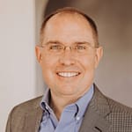 Man wearing glasses and a sports coat smiles warmly