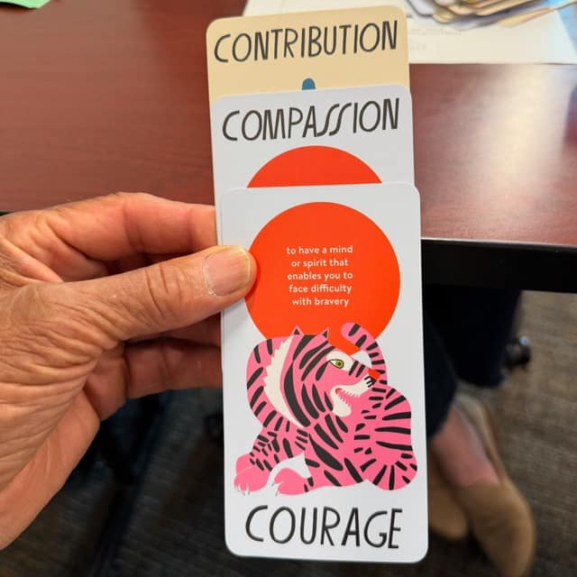 Person holds three cards: Contribution Compassion Courage