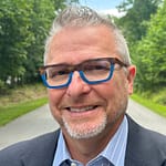 Man wearing glasses with a slight beard smiles at the camera