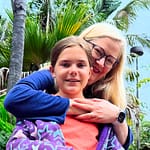 A mom hugs her daughter while standing behind her