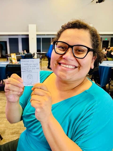 Smiling woman holds up a hand drawn card with a self portrait that reads: "I give myself permission to draw things and not care what anyone thinks."