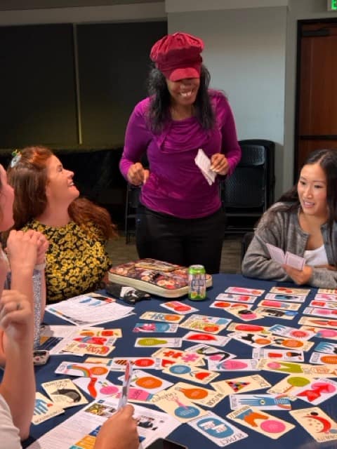 Women laugh together in front of a table full of cards with values written on them.
