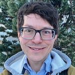 Man with dark brown hair, wearing glasses and a grey hoodie